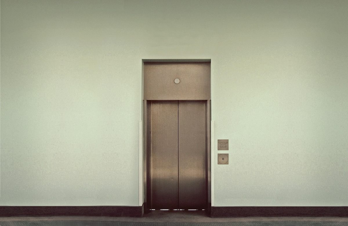 Porte d'ascenseur métallique encadrée par un mur clair et deux interrupteurs Porte d'ascenseur métallique encadrée par un mur clair et deux interrupteurs