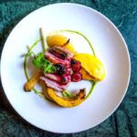 Assiette blanche contenant magret mangue baies feuille sur fond vert